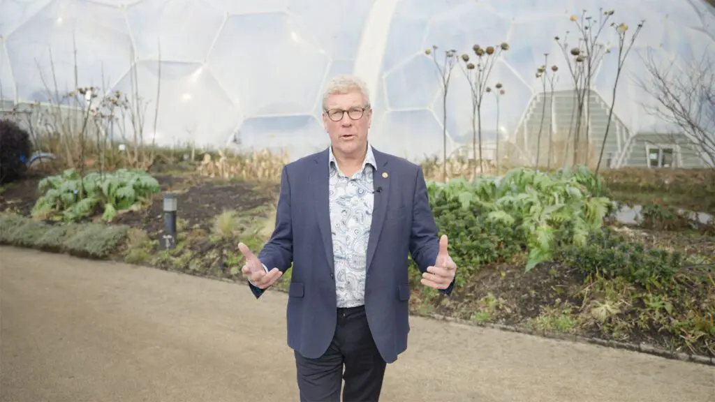 Man stood on paths in front of Eden Project biomes, looking t camera