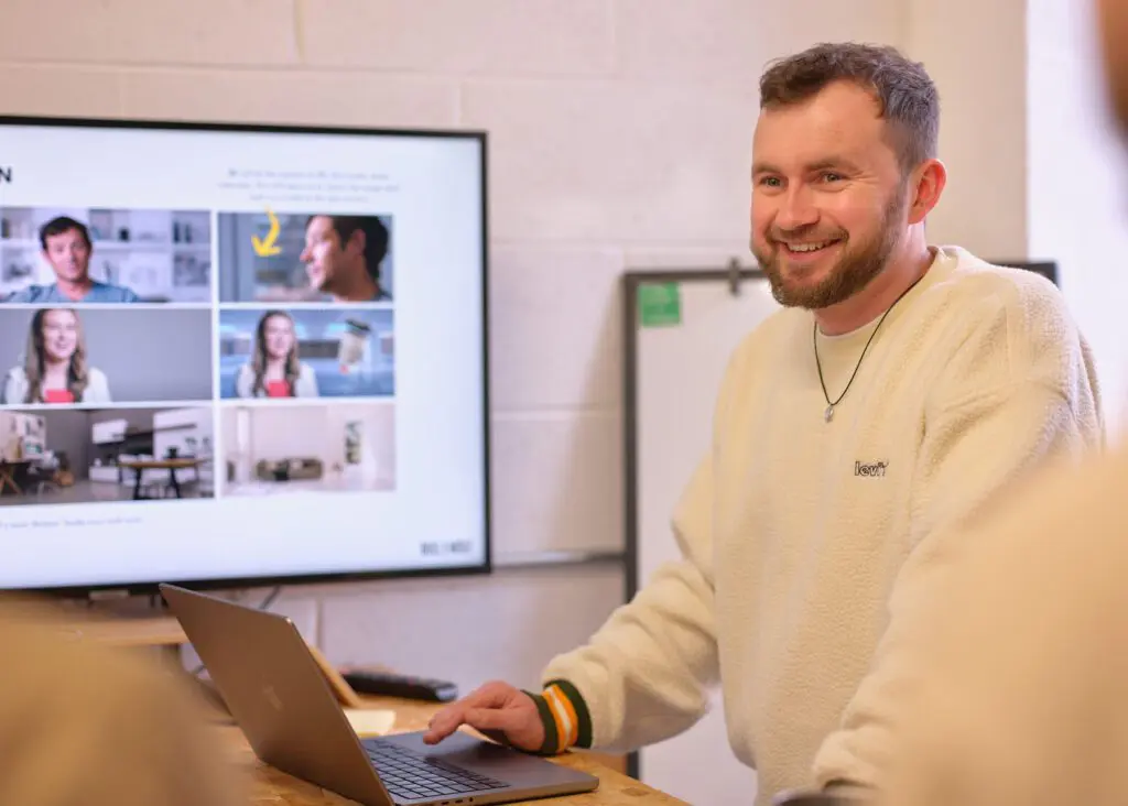 Joe stood at laptop smiling at someone across the desk