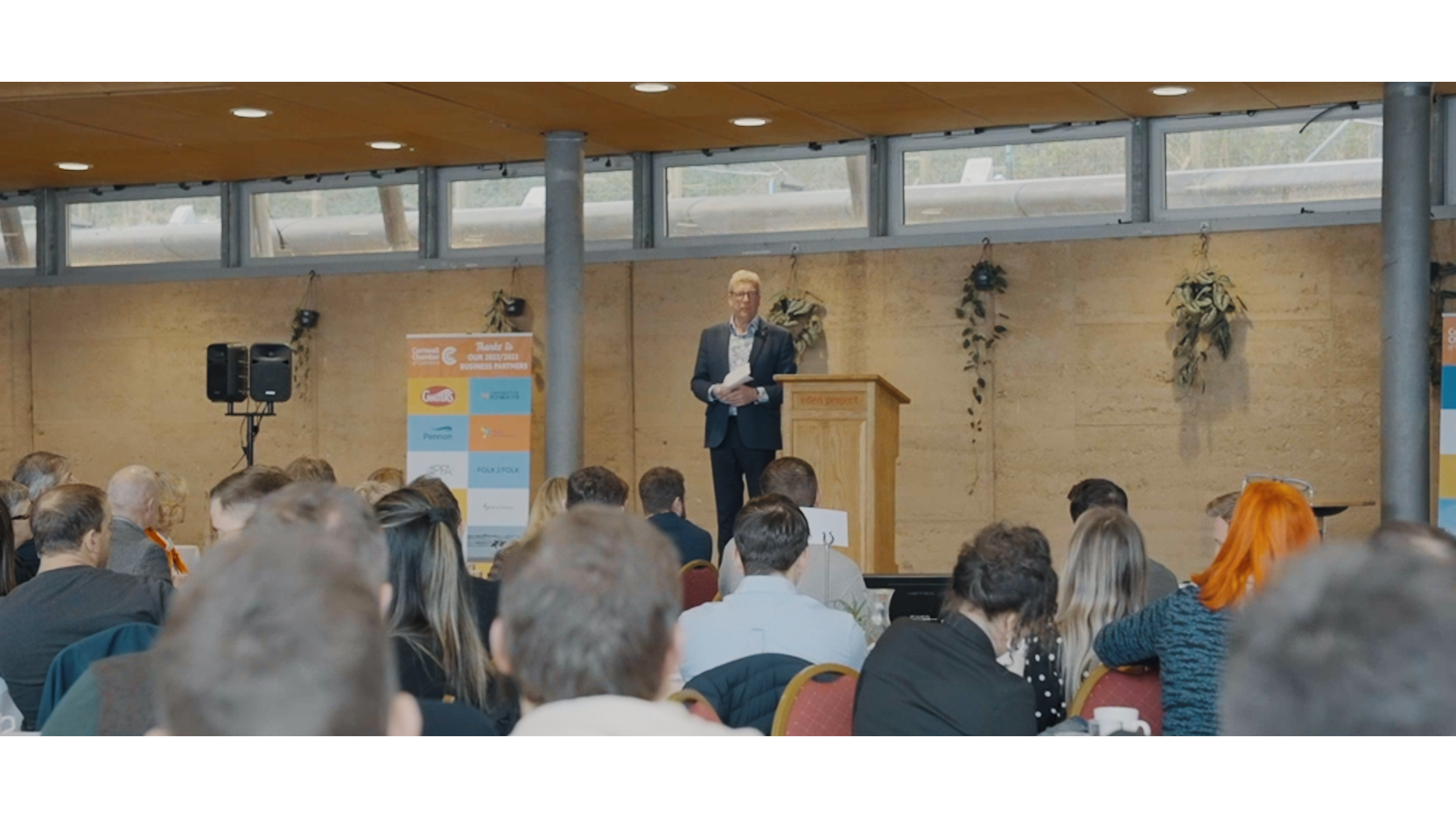 Man stood on stage talking to a crowd of people, Bull and Wolf filming the Event Video Production