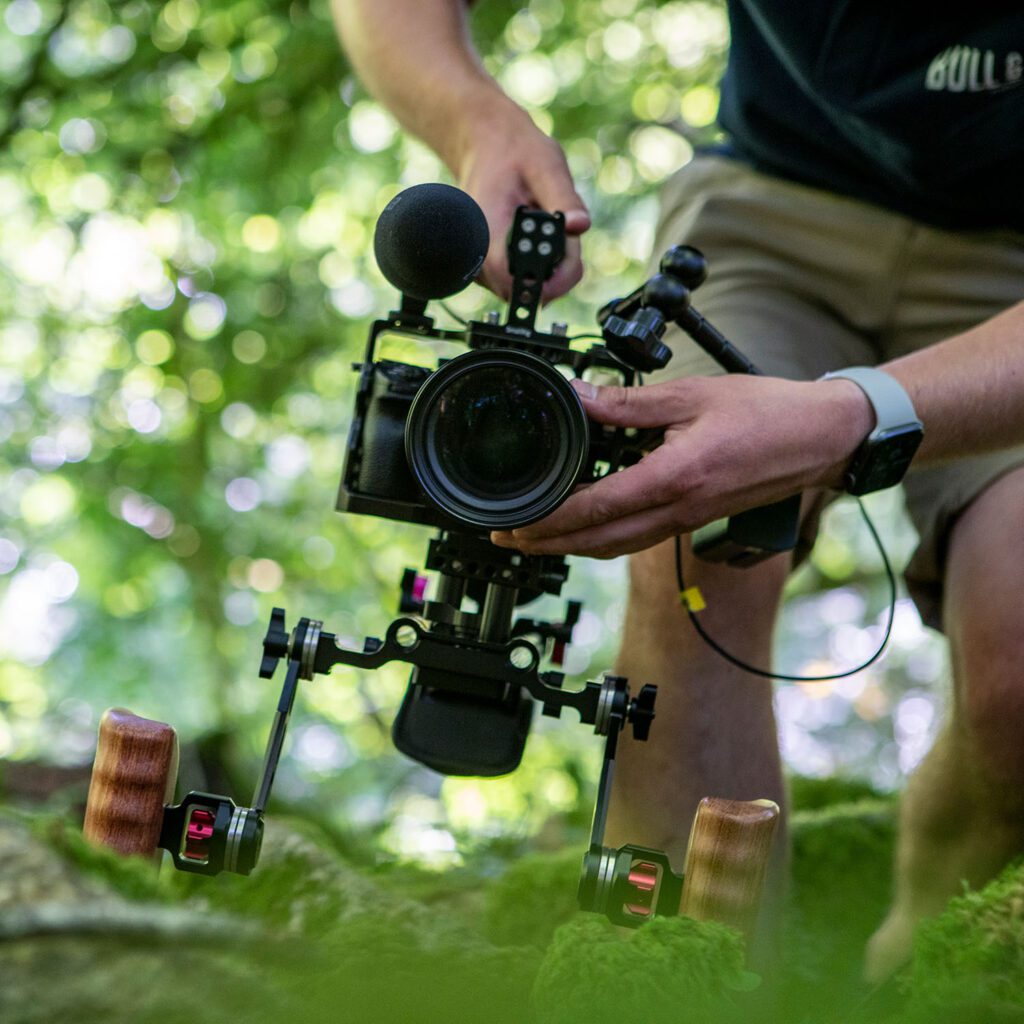 Front view of a man holding a camera in woods, filming