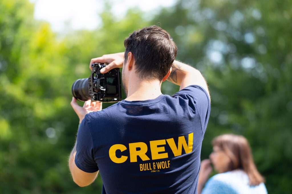 Behind shot of cameraman in Crew Bull & Wolf t-shirt holding camera