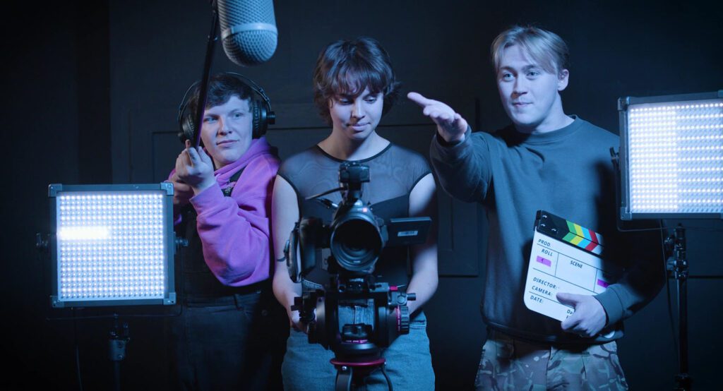 Three students one holding clapperboard, one holding camera and other holding sound mic.