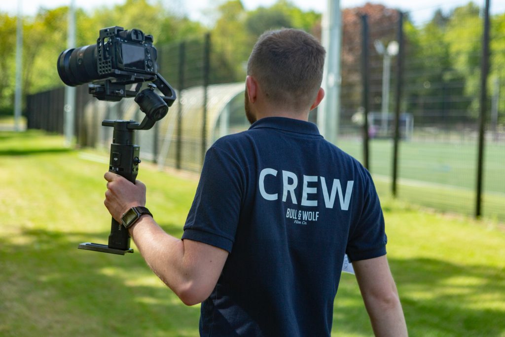 Cameraman wearing a crew t-shirt holding a camera and walking away